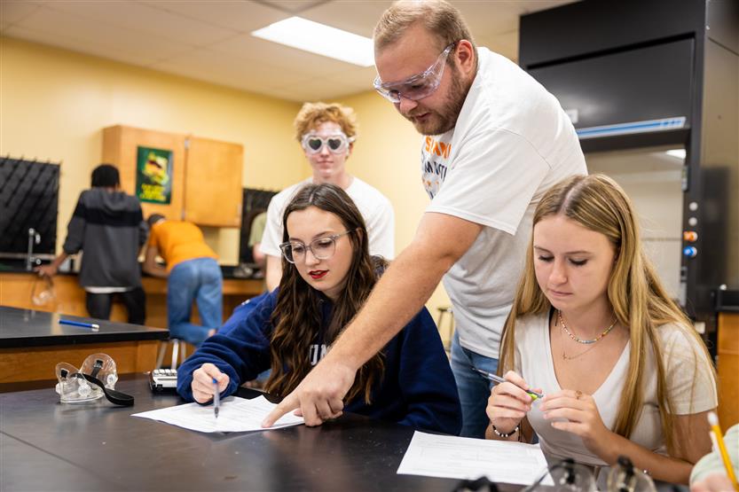 A teacher helps two students during a lab